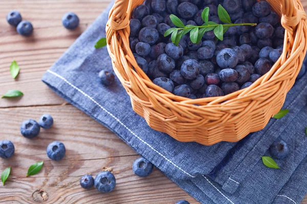 Friss áfonya kosárban, zöld levelekkel, fából készült asztalon.