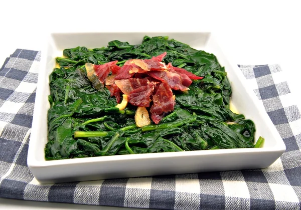 Fagyasztott spenót tálalva, gazdag zöld színnel és sonkával a tetején.