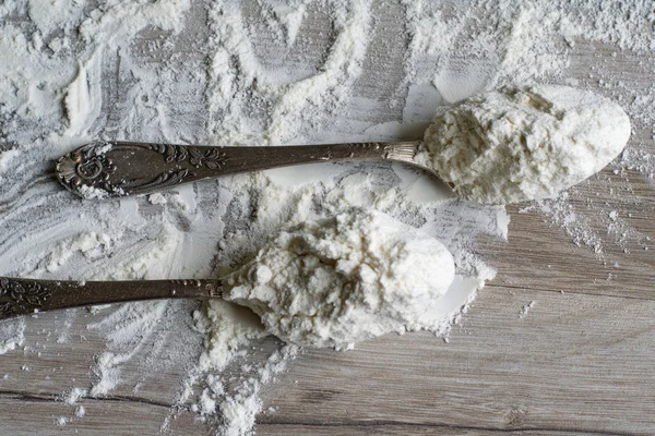 Két evőkanál liszt, egy fakanálon, konyhai munkafelületen.
